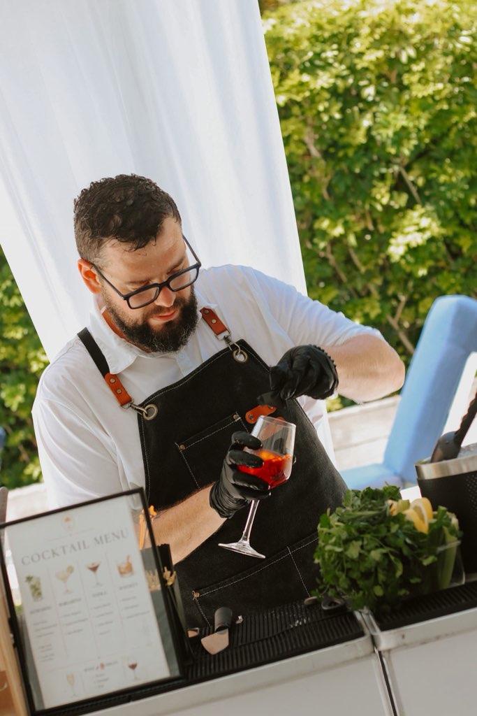 Miami bartender garnishing an Aperol Spritz at an outdoor garden event